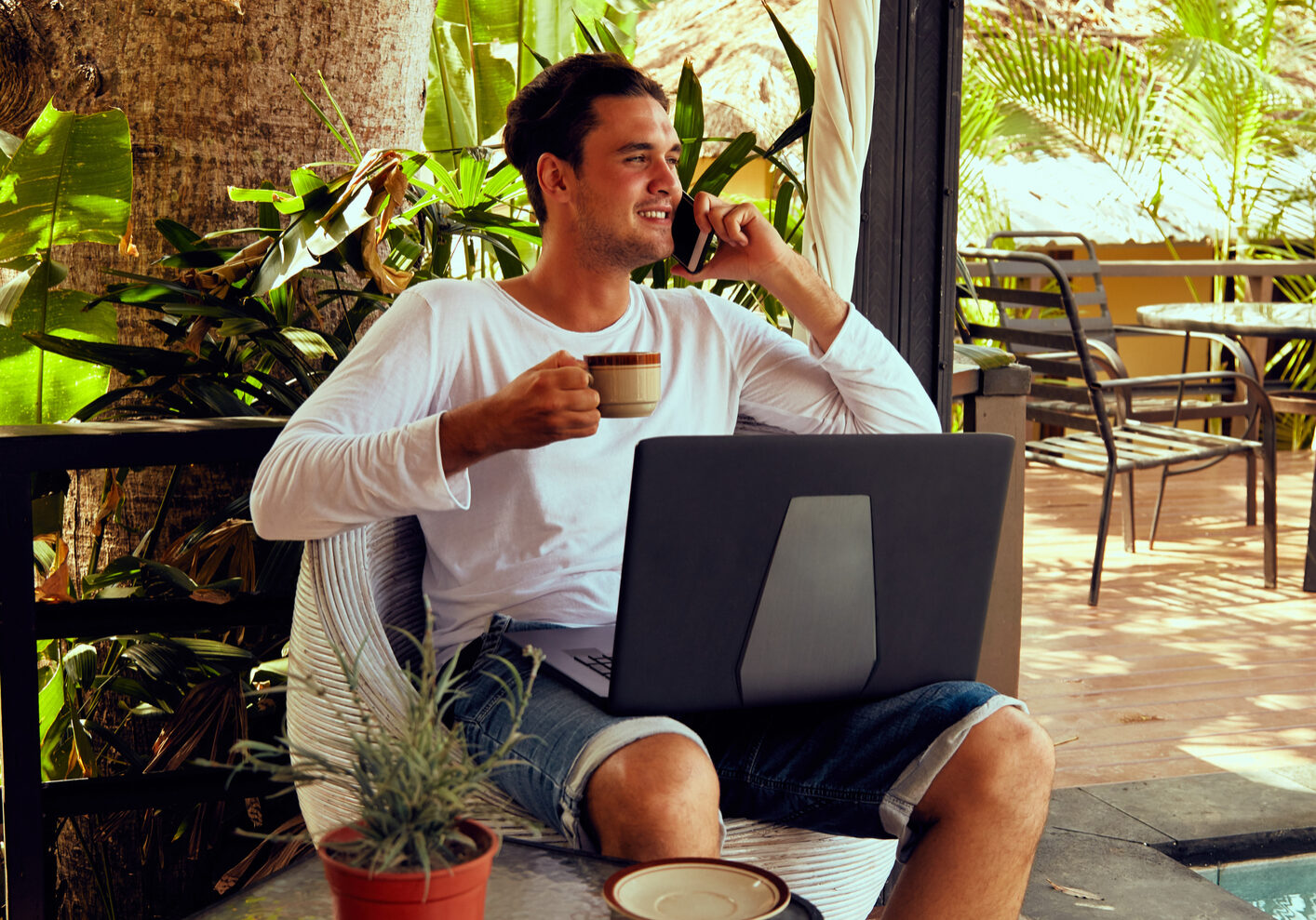 Man using cellphone while working on laptop outdoors.